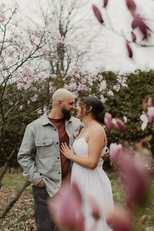 A romantic couple embraces under blooming cherry blossoms in a spring garden setting.