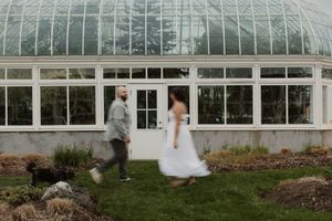 Newlywed couple embraces in front of a white greenhouse with glass panels on their wedding day.