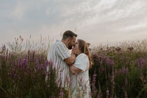 A couple shares a romantic moment in a field of purple wildflowers at sunset.