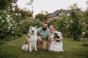 A husky and a small dog pose with their owners in a lush garden setting.