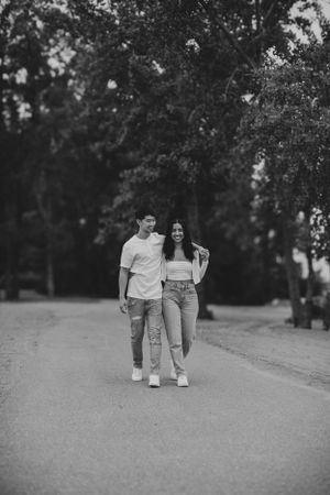 A couple walking together on a tree-lined path in casual attire, captured in black and white.