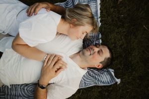 A couple lying together on a blanket outdoors sharing an intimate moment.