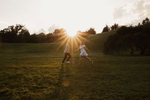 Two people running through a grassy field at sunset with dramatic sunburst.