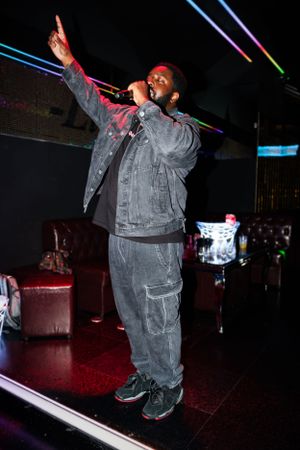 Performer in denim jacket gesturing while singing on nightclub stage.
