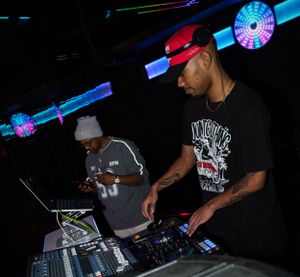 DJs mixing music at turntables in a dark nightclub with neon lights.