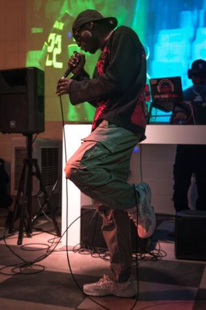Performer on stage with microphone in dramatic lighting with green and blue backdrop.