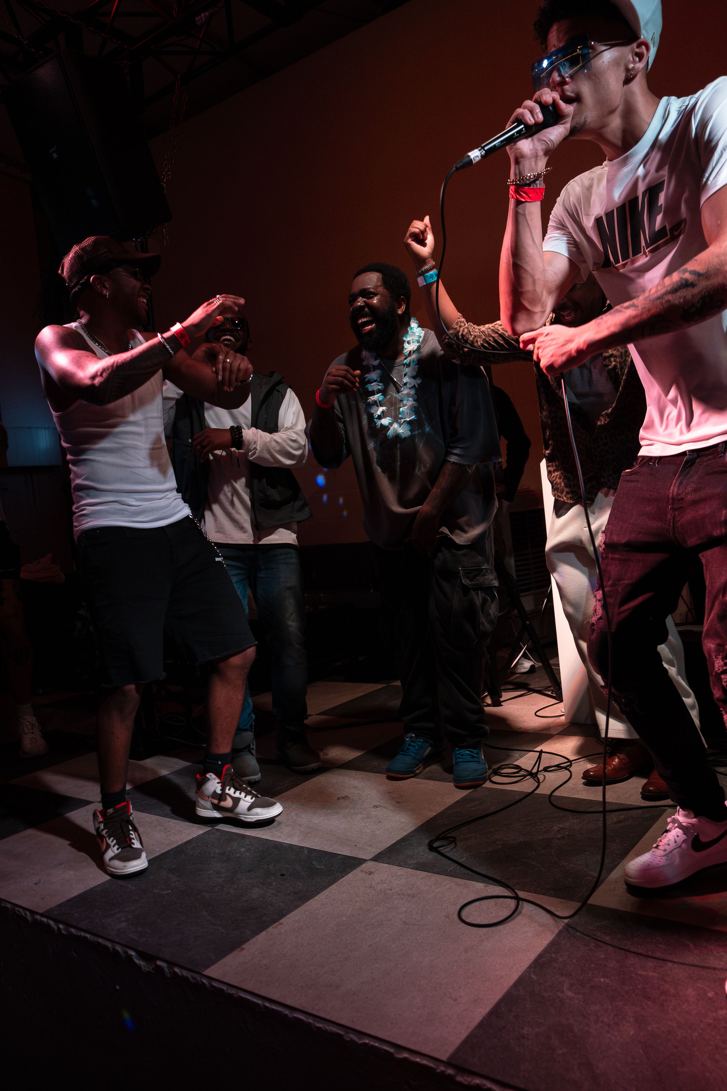 Group of performers energetically singing and performing on checkered stage.