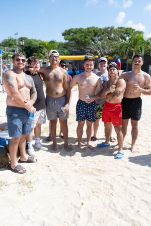 Group of friends posing together on a sunny beach with palm trees in the background.