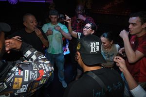 People gathered in a dark room looking at their phones, some wearing baseball caps and casual clothing.