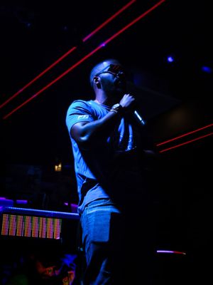 Performer singing on dark stage illuminated by blue lights and red laser beams during nighttime concert.