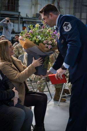Military service member in dress blues presents a beautiful bouquet of flowers during ceremony.