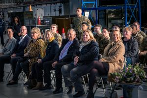 Audience members seated in rows at formal military event in industrial setting.