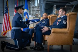 Military personnel in dress blues engage in formal conversation with American flag in background.