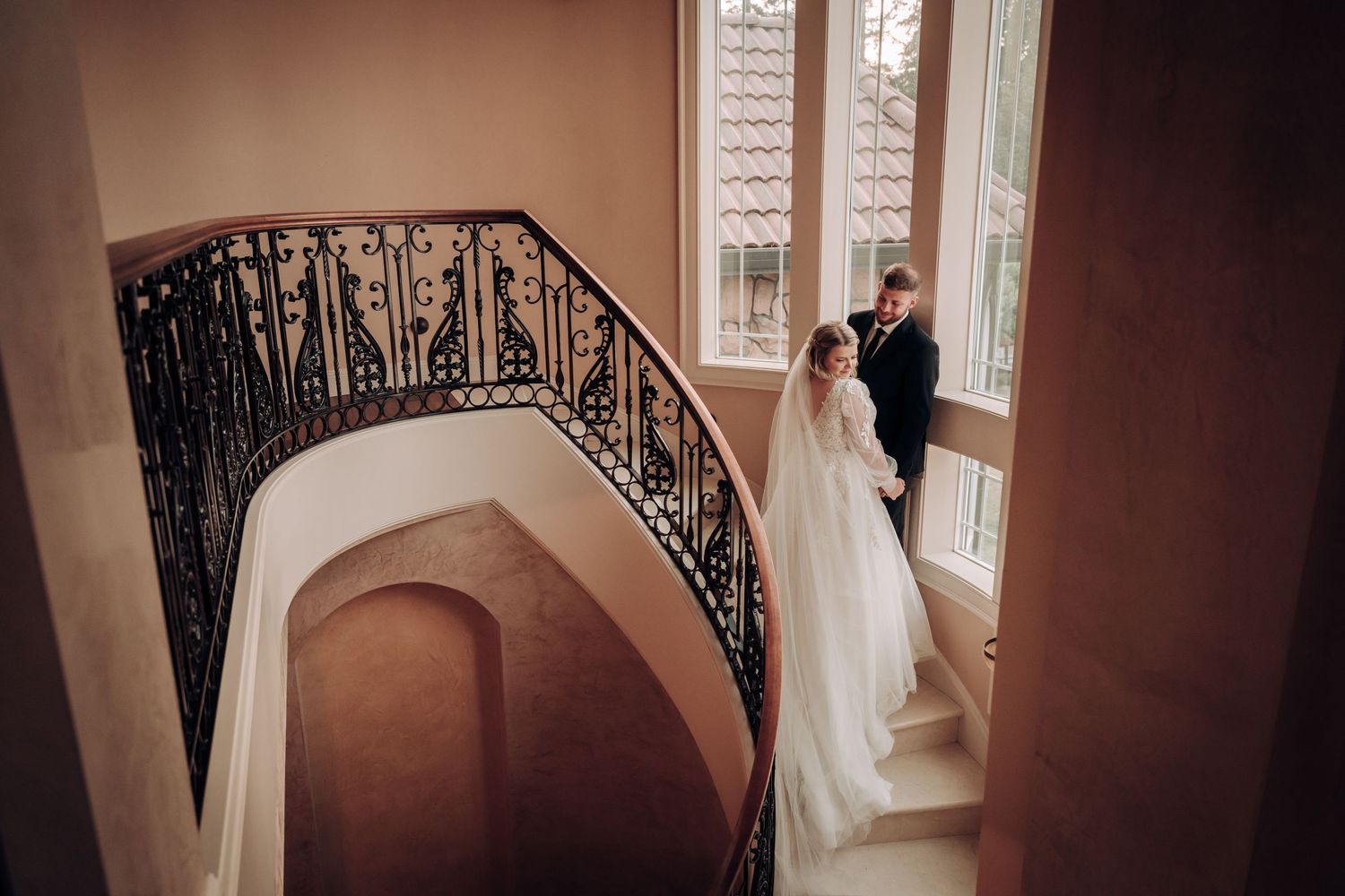 Elegant wedding photo on grand staircase with ornate iron railing.
