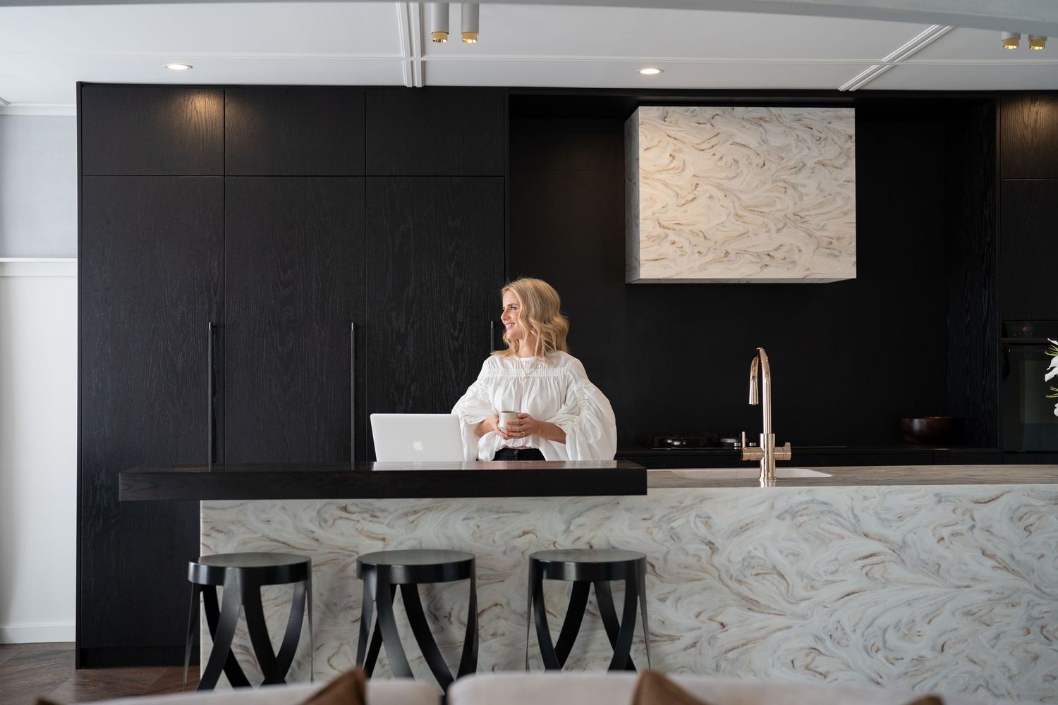 Modern kitchen interior with dark cabinets, marble backsplash, and contemporary pendant lights over a sleek island.