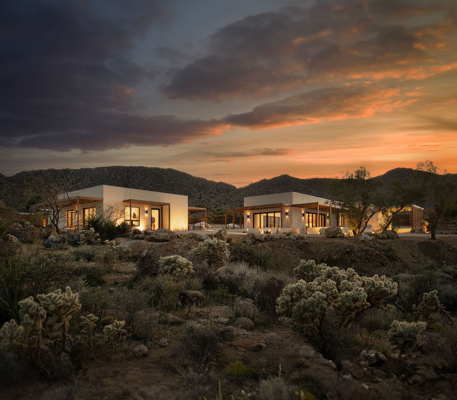 Desert modern homes nestled in rocky terrain under dramatic sunset sky.