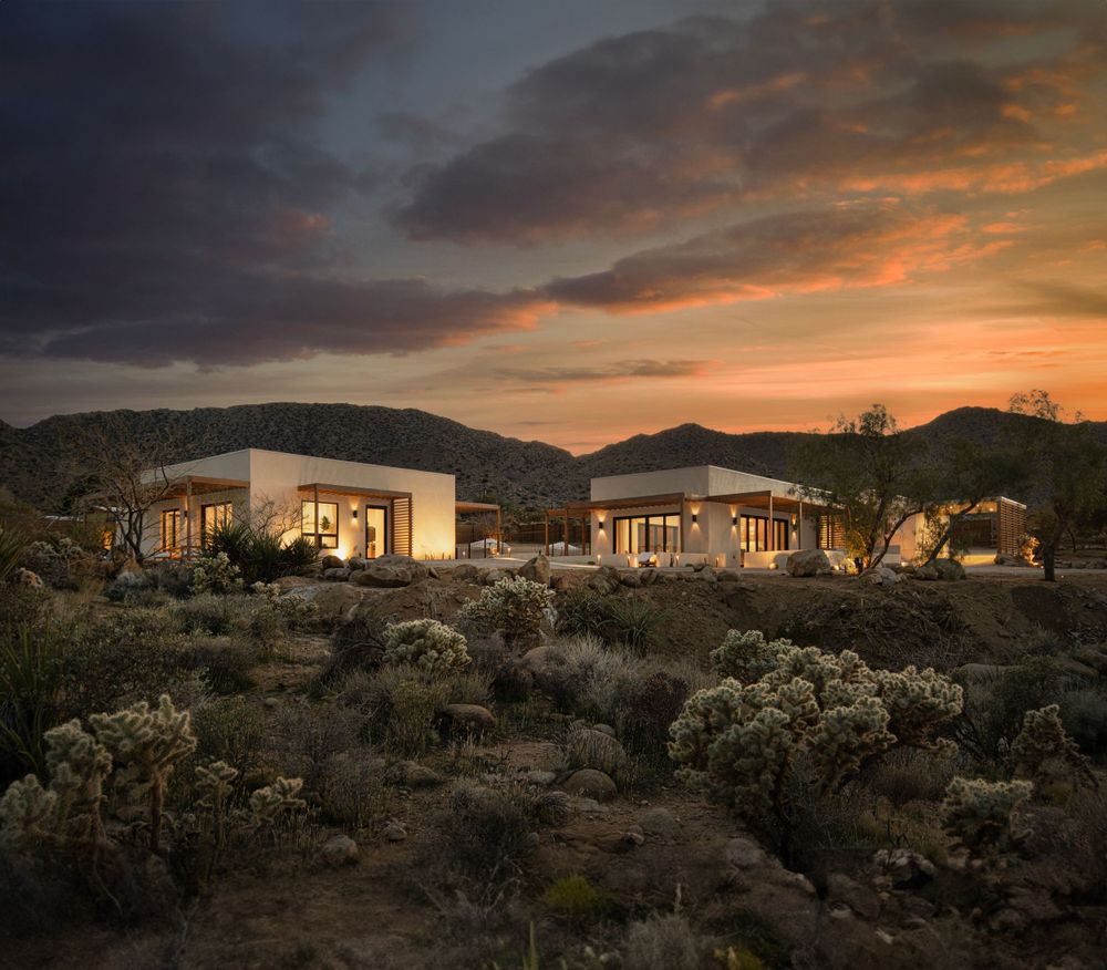 Desert modern homes nestled in rocky terrain under dramatic sunset sky.