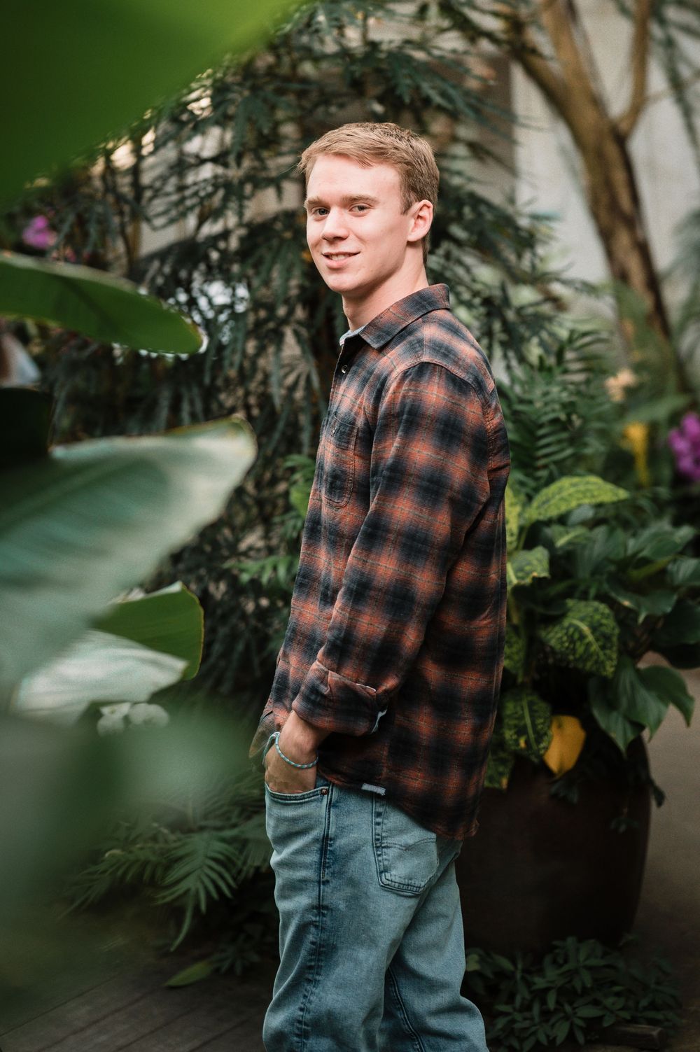 Casual portrait in plaid flannel shirt surrounded by indoor plants and greenery.