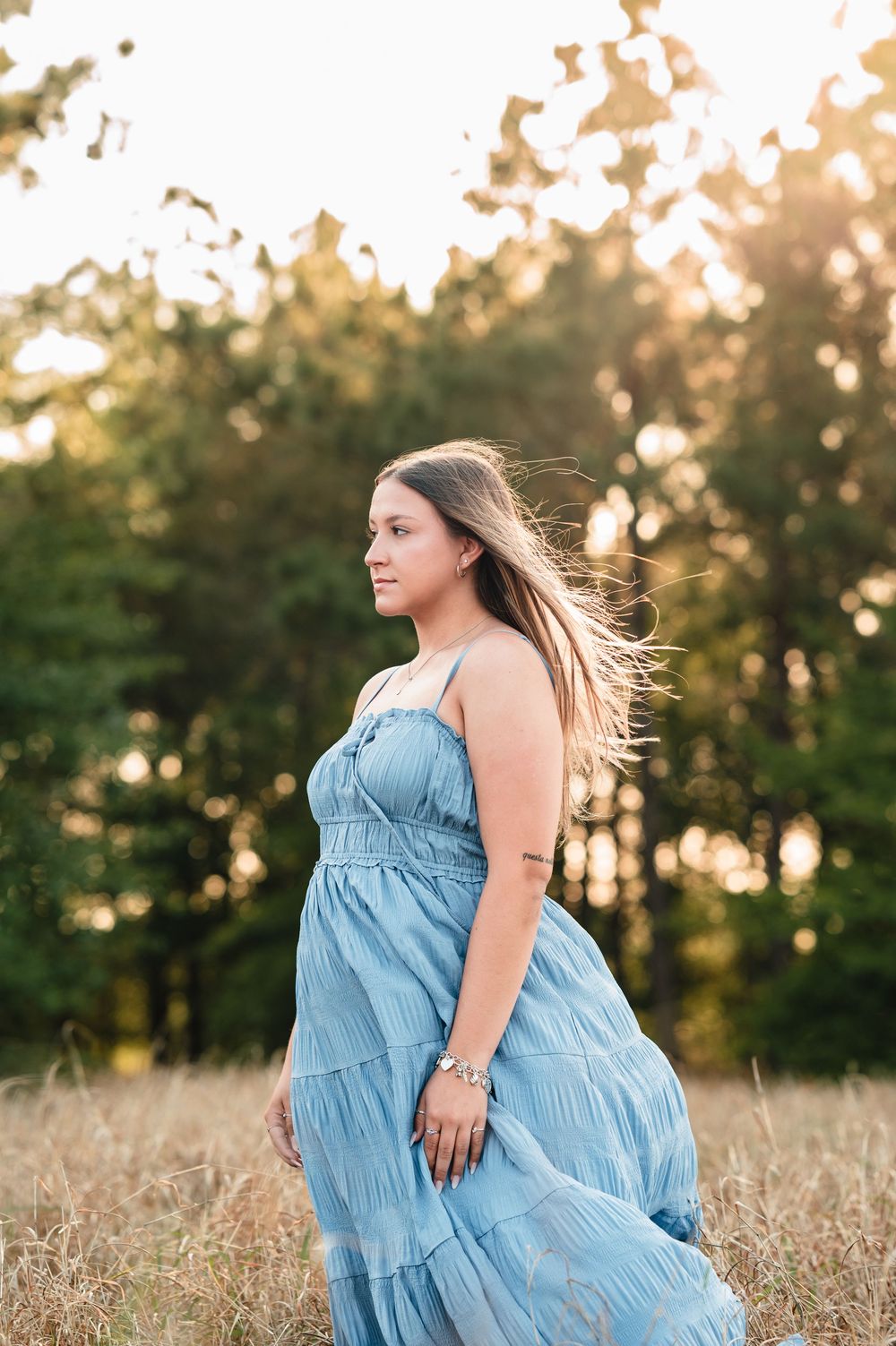 Woman in flowing blue dress twirling in golden sunlit field at sunset.