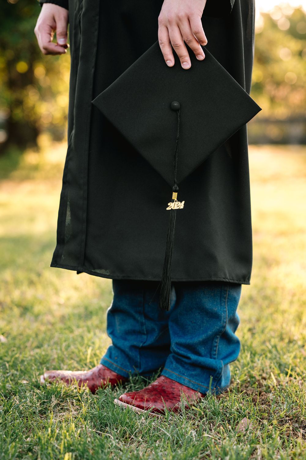 Close-up of graduation cap and tassel with black graduation gown against sunset background.