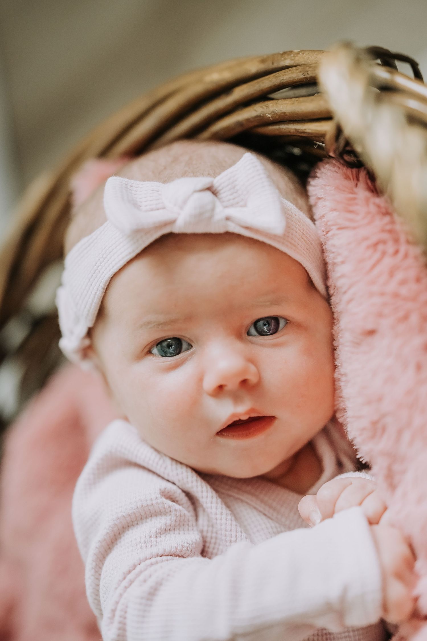 Baby wearing white bow headband and knit outfit against pink blanket.