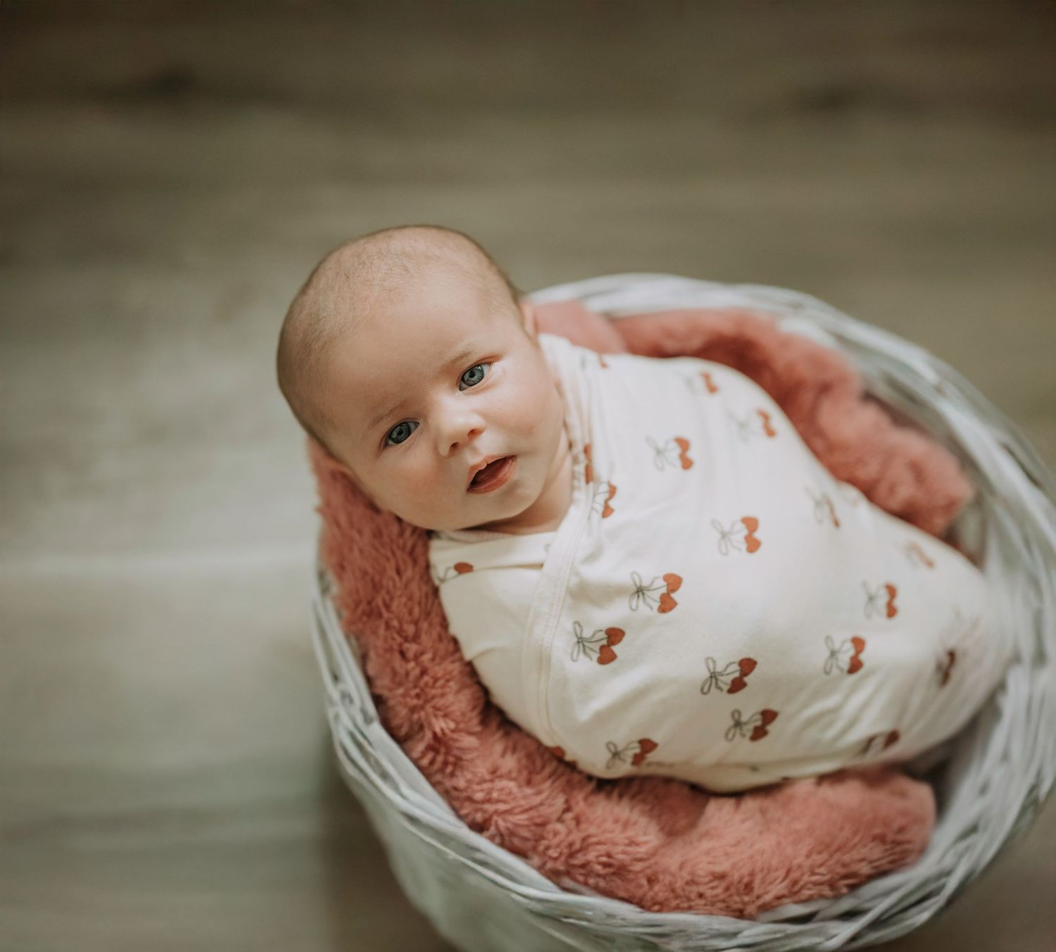 Newborn resting peacefully in white basket with pink cushioning.
