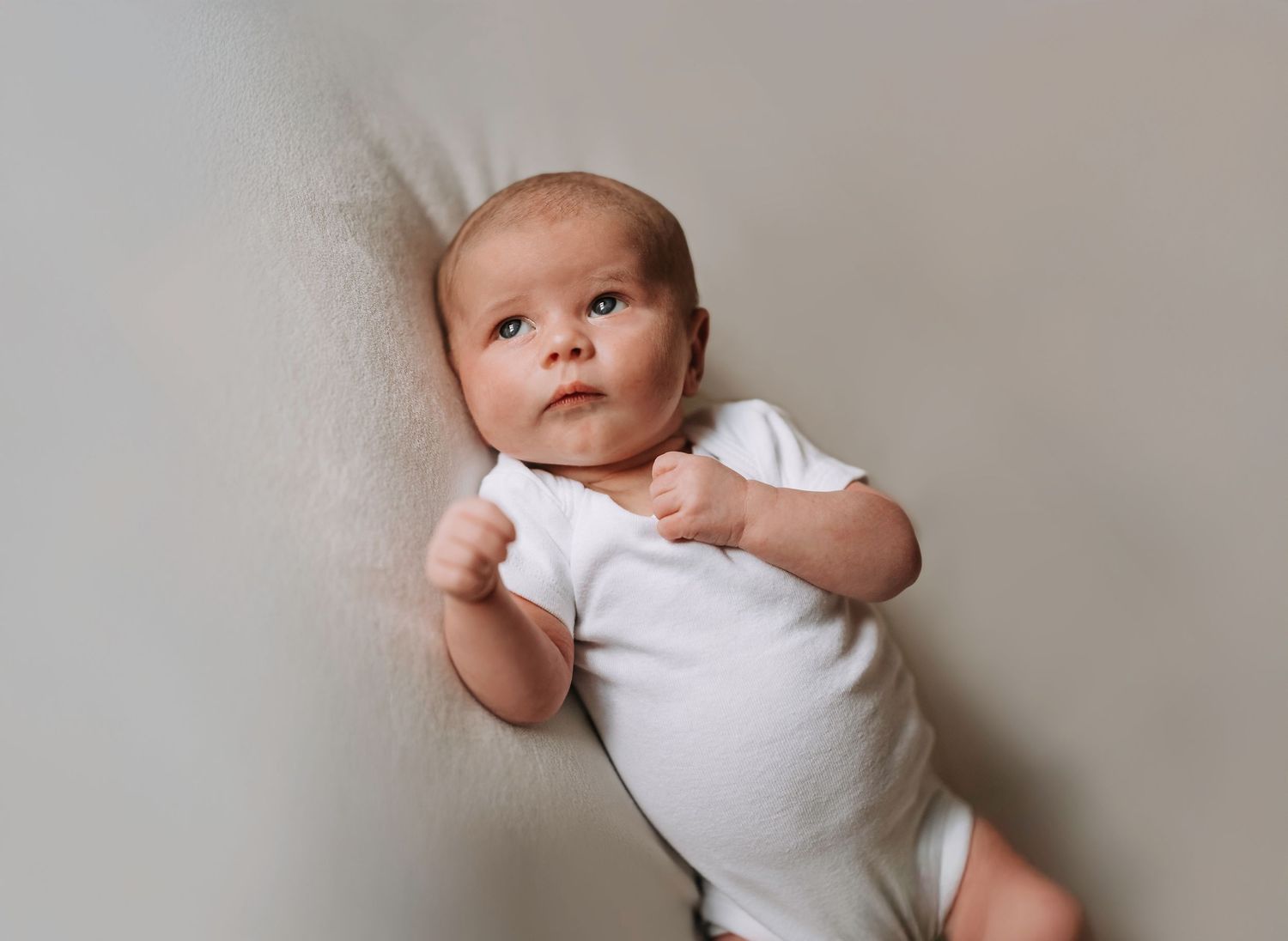 Baby in white onesie lying on light gray backdrop.