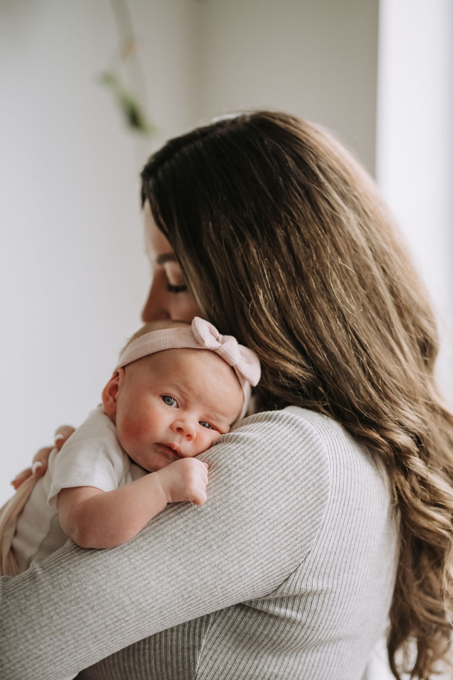 Baby in white bow resting on shoulder against neutral background.