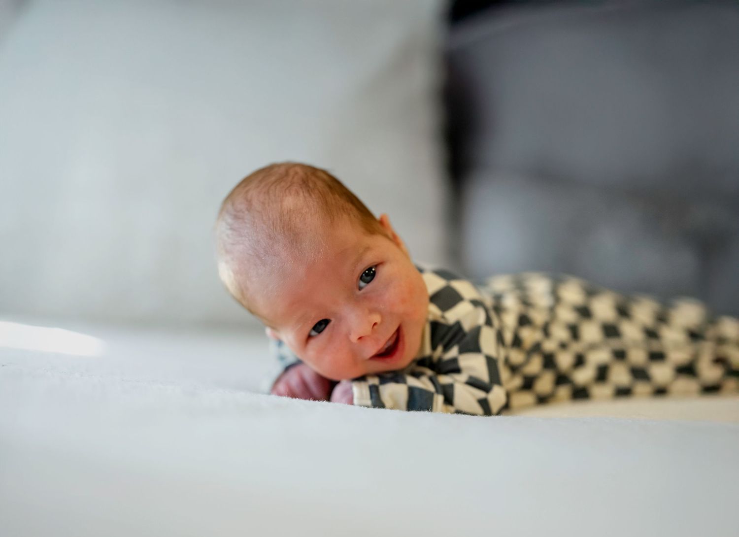 Newborn baby sleeping peacefully on white bedding with checkered pattern detail.