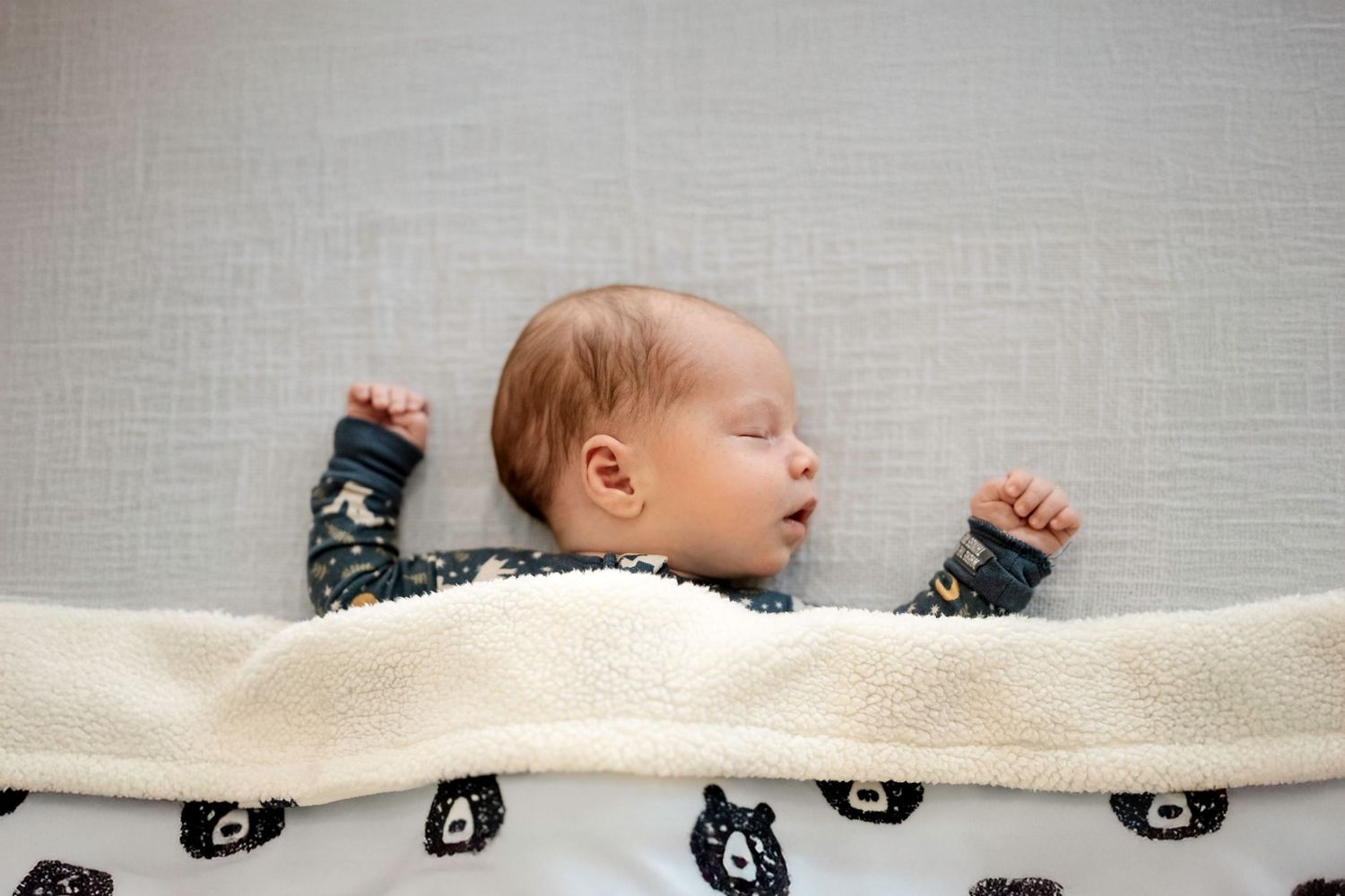 Newborn baby wrapped in a cozy white blanket with black bear pattern.