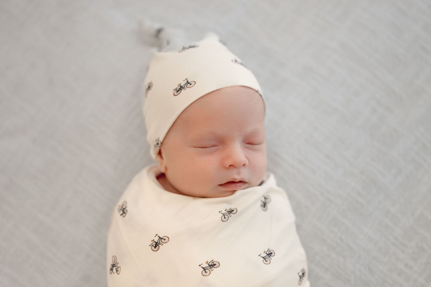 Sleeping newborn wearing a delicate white outfit on gray background.