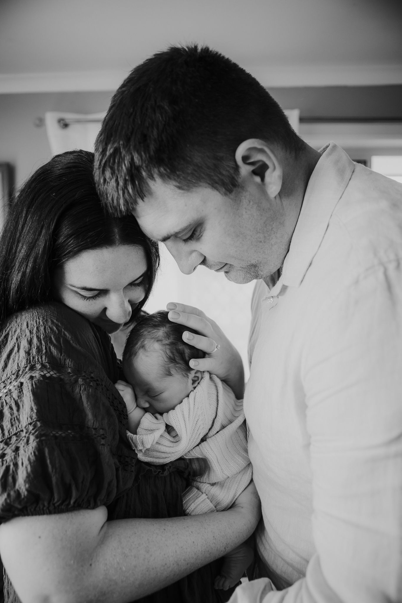 Black and white photo of parents tenderly cradling sleeping newborn baby together.