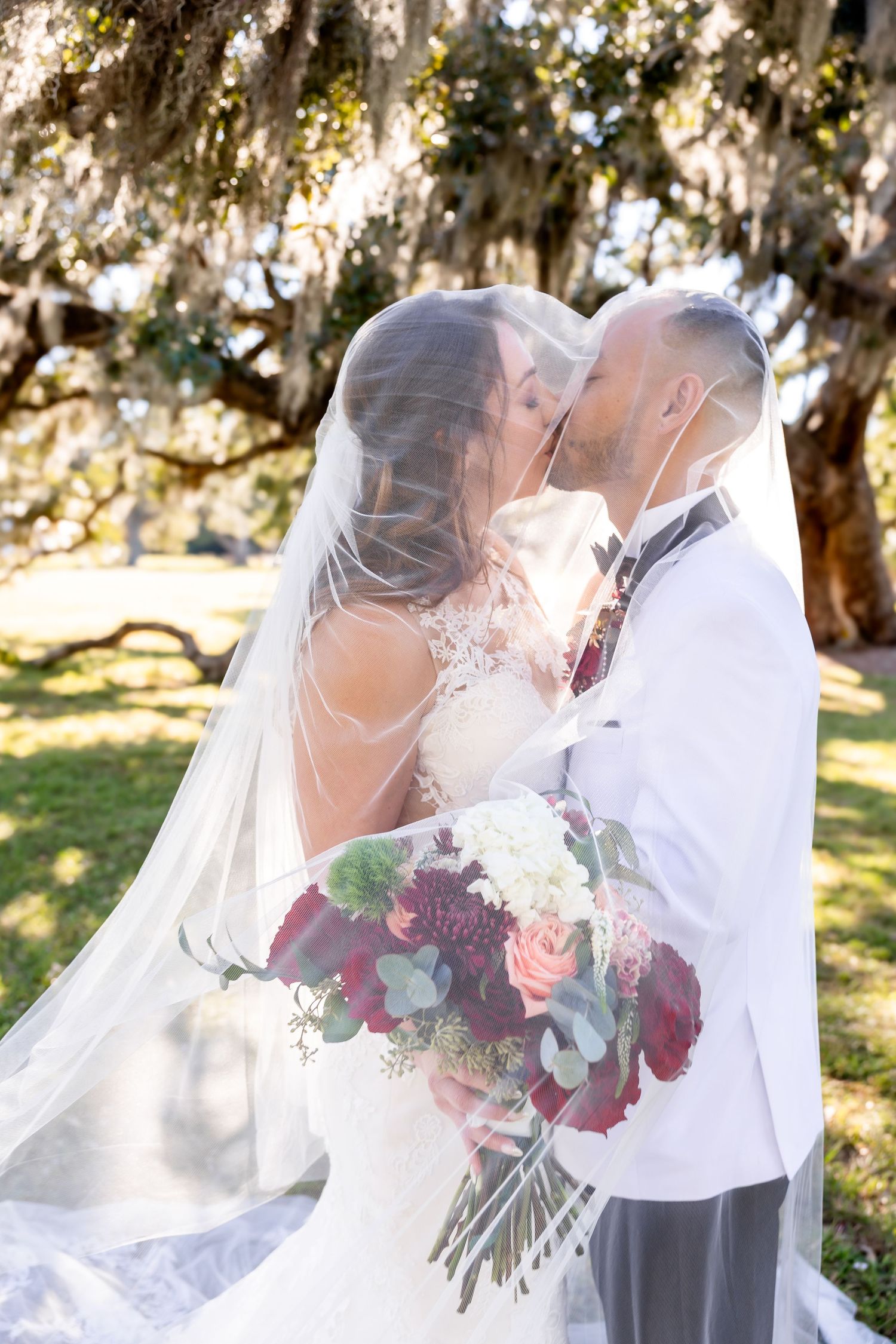 Black and white photo of bride and groom nearly kissing with flowing veil in breeze.