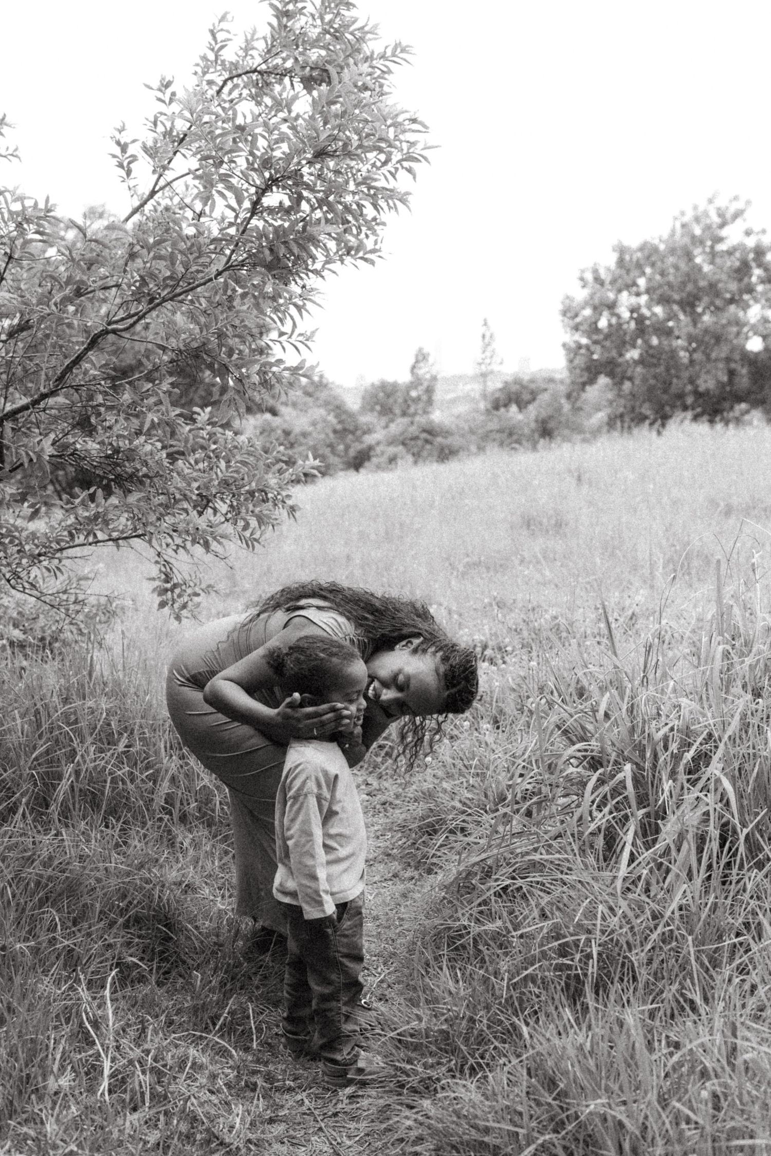 Black and white photos of people bending down to examine something in tall grass.
