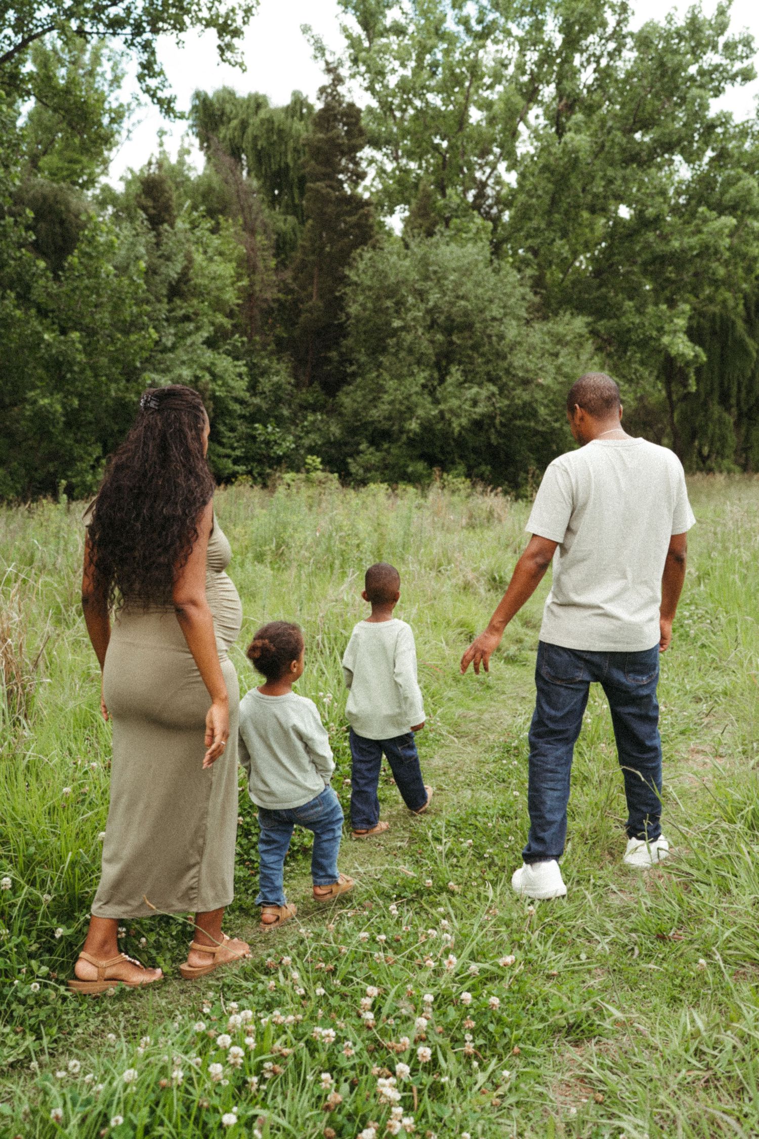 Family walking together through a summer meadow with wildflowers and trees.