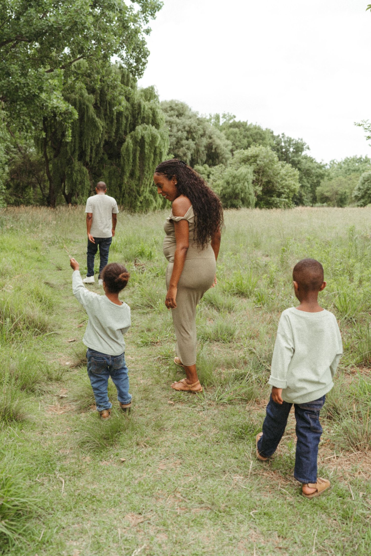 Family walking together in a grassy field with willow trees in the background on a sunny day.