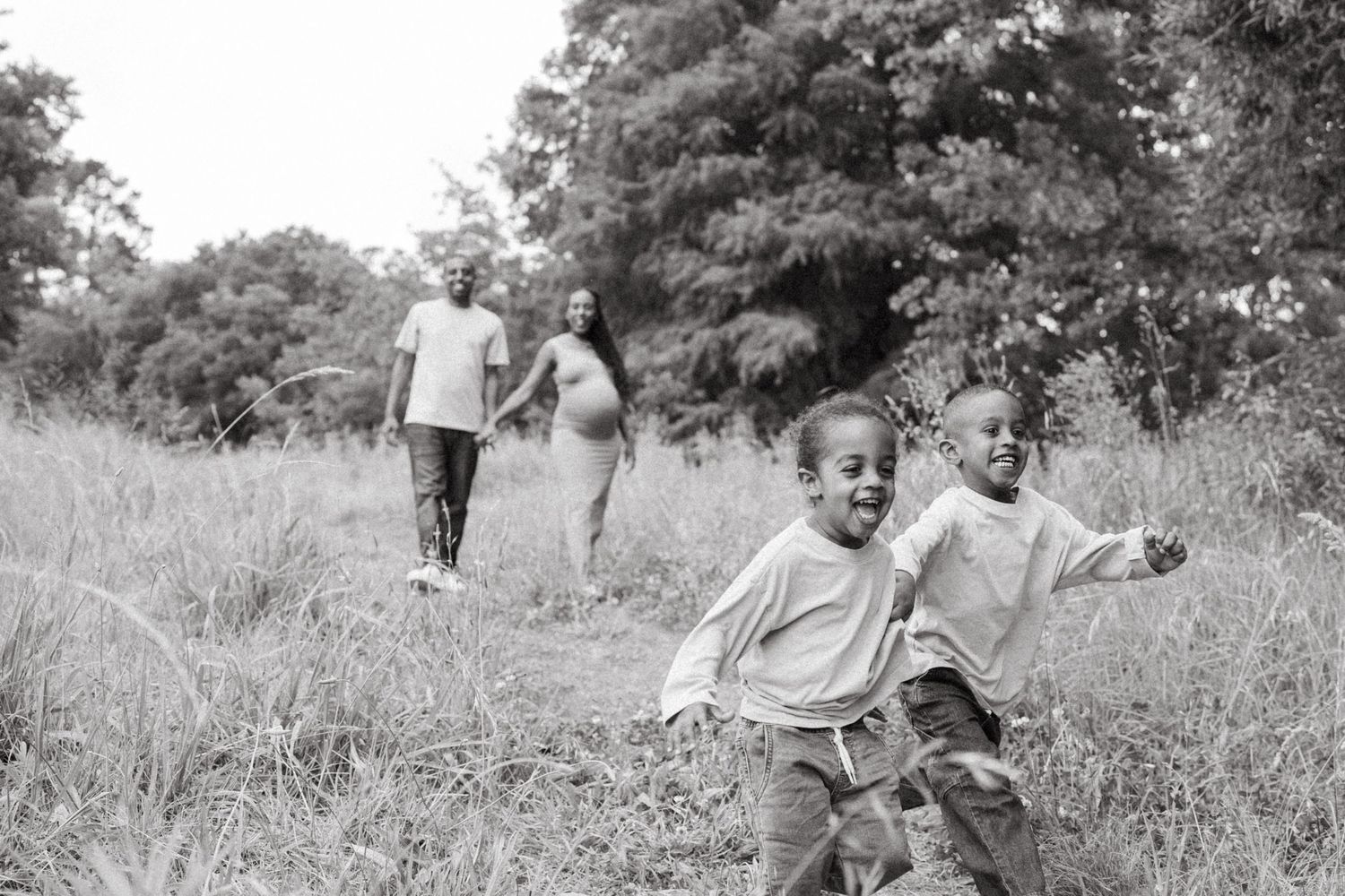 Black and white photo of children running joyfully through a meadow while adults walk ahead.