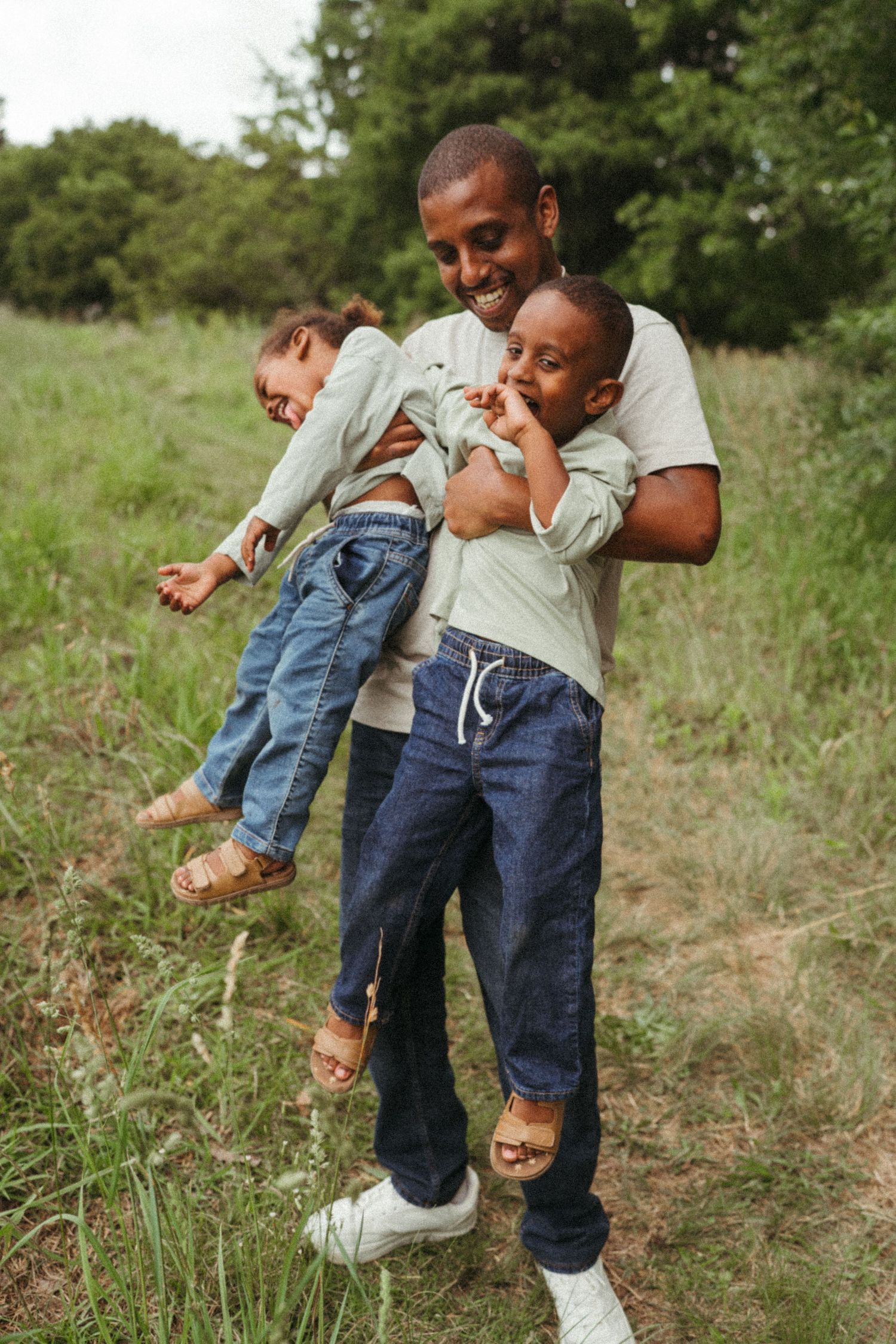 Playful moment in a grassy field as adults lift and swing children.
