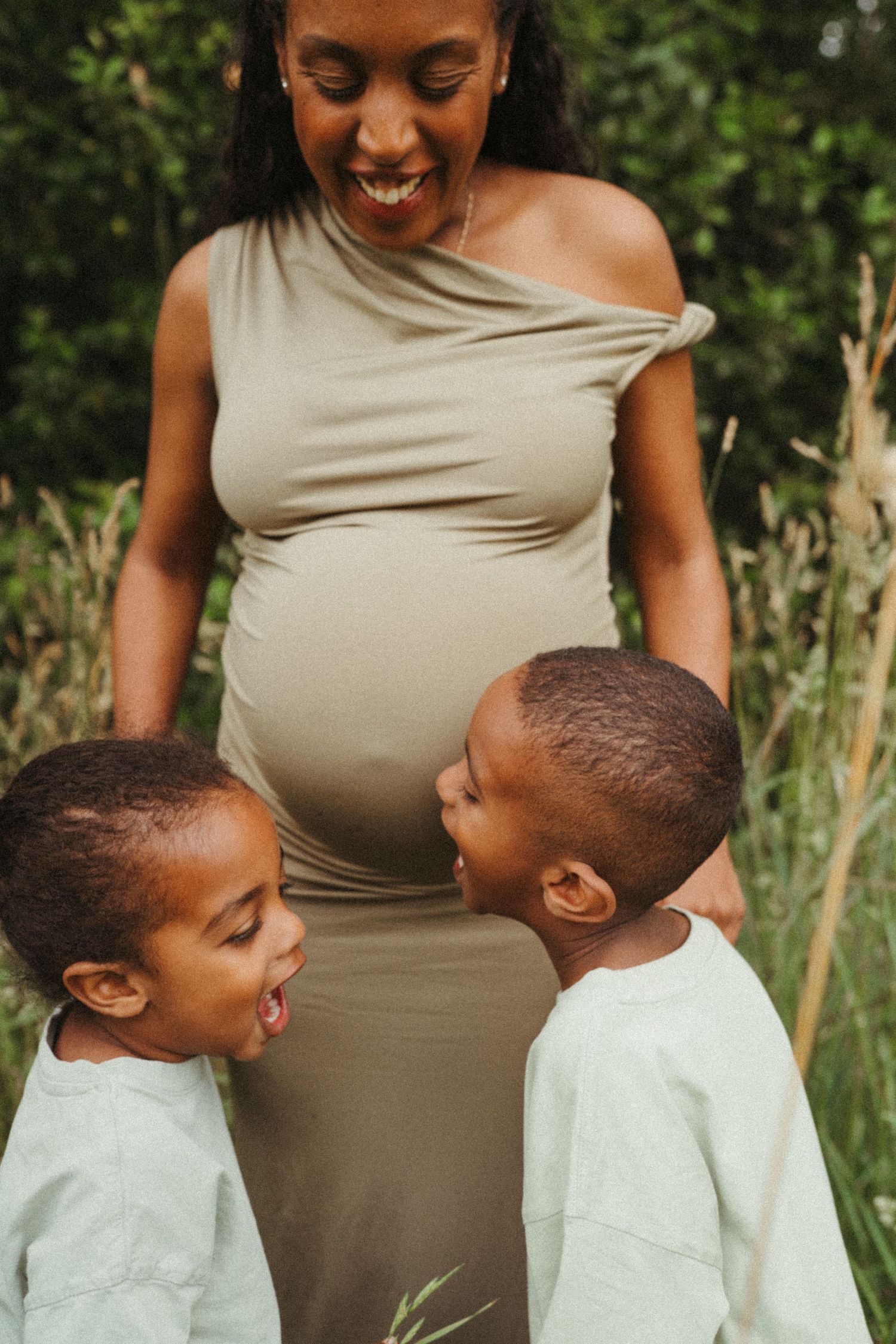 Candid moment of children laughing with expectant mother in a natural outdoor setting.