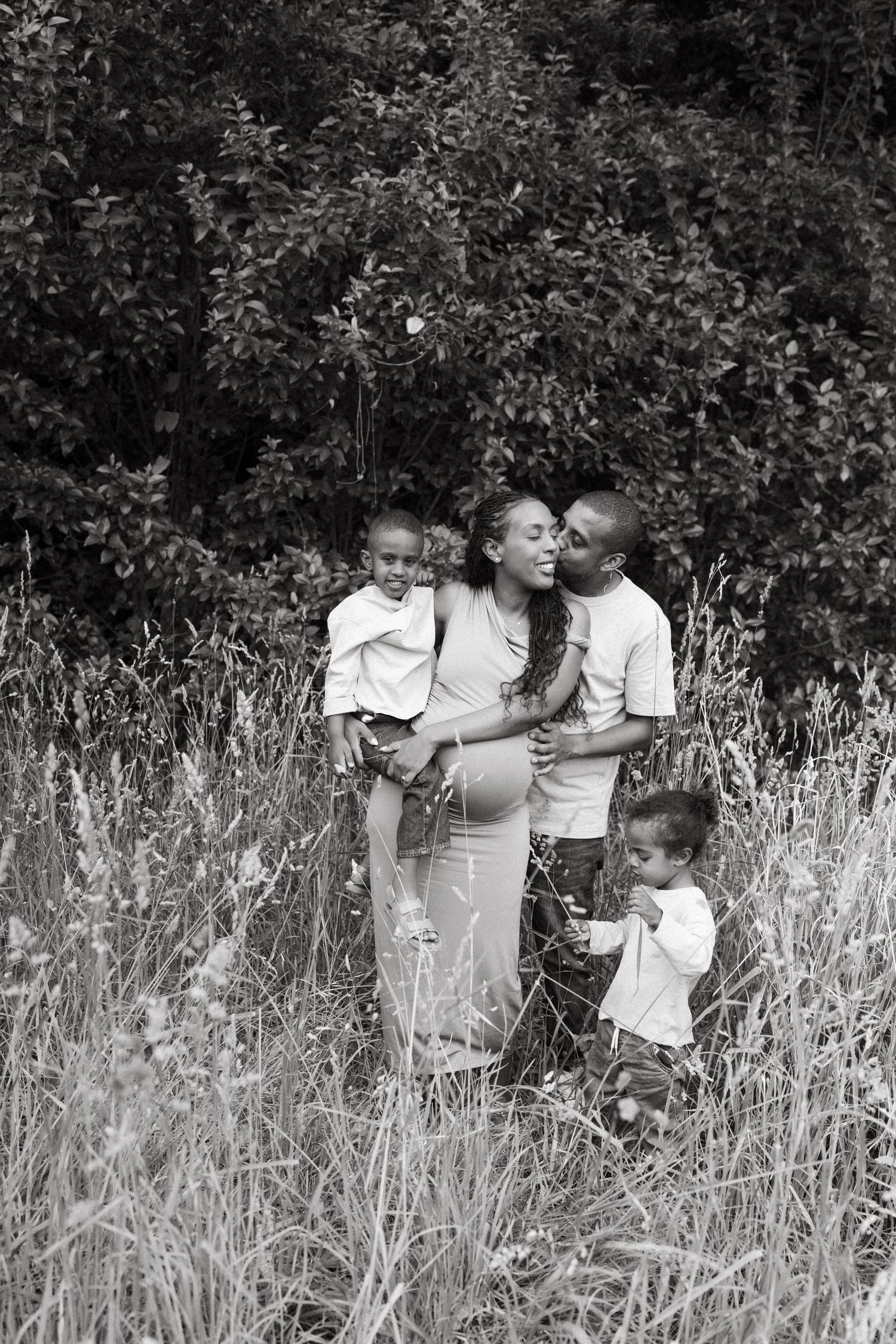 Black and white portrait of a family embracing in a field of wild grass.
