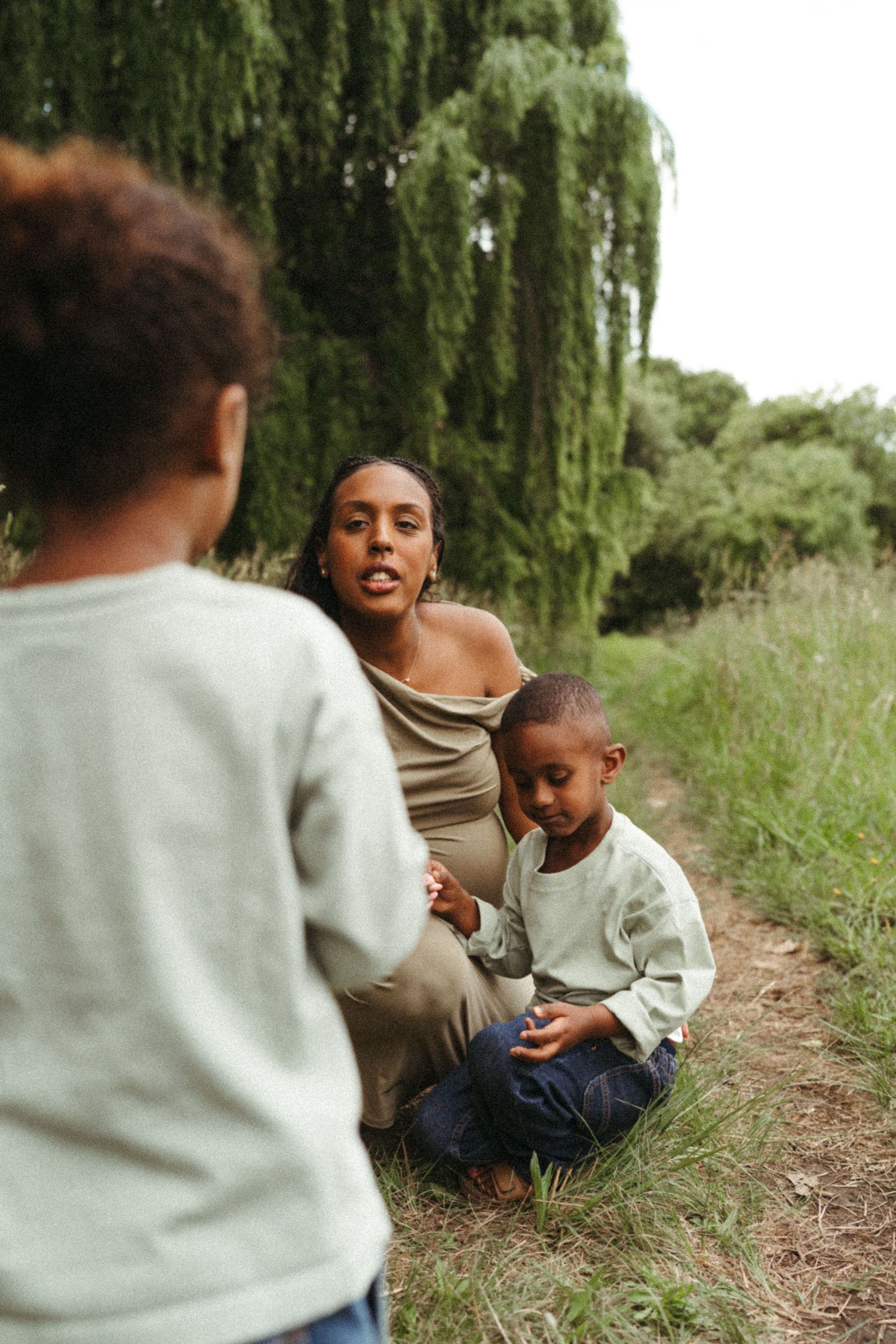 Parent and child having a playful moment outdoors near willow trees.