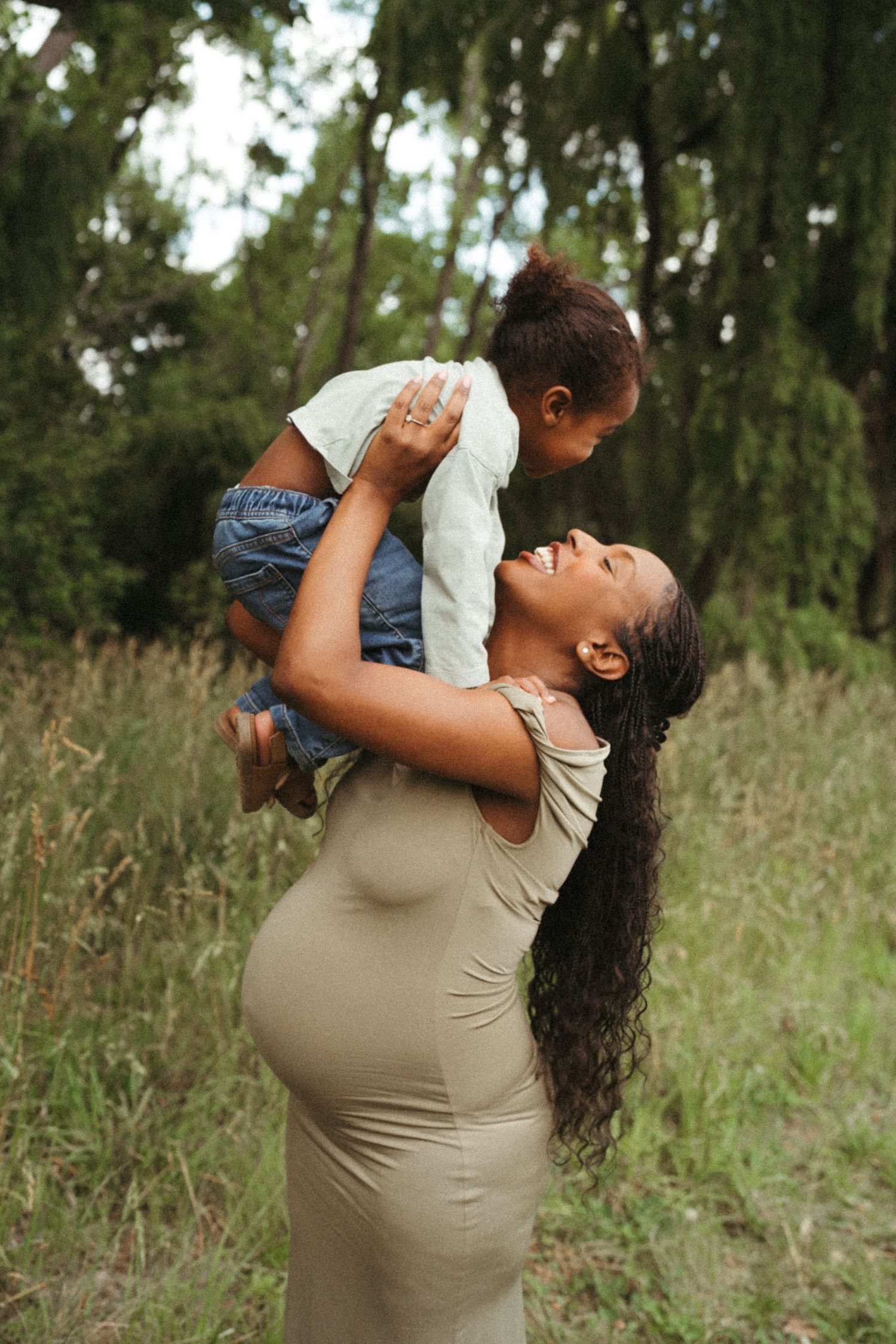 Tender family moment captured in a grassy field with willow trees in background.