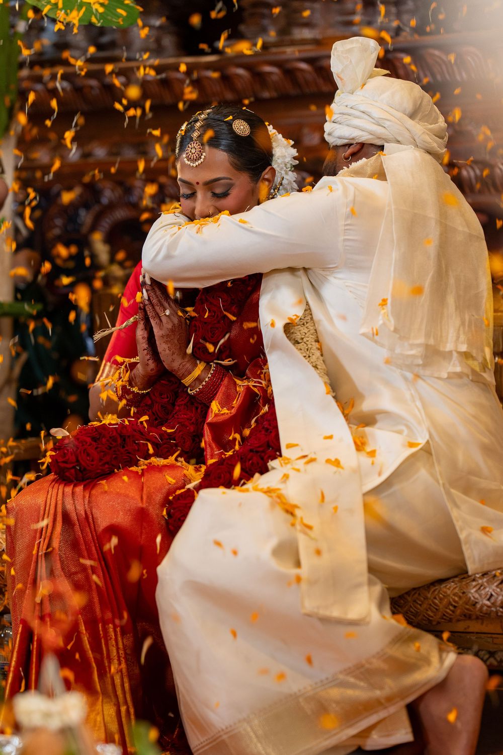 Traditional Indian wedding ceremony with couple in red and white attire as flower petals fall during a ritual moment.