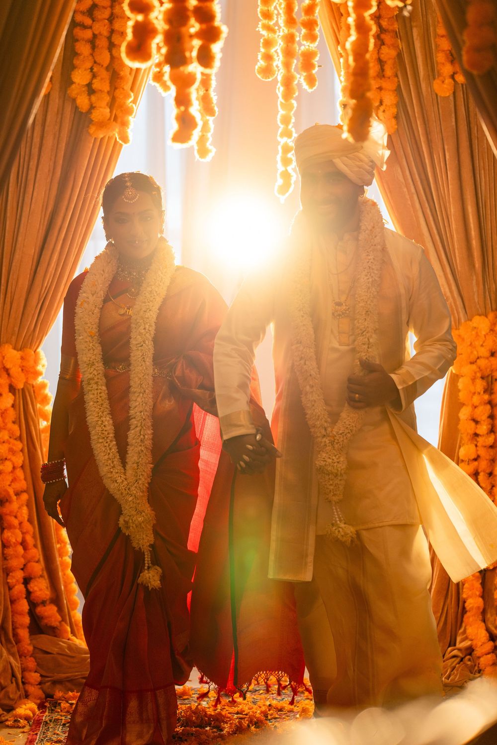 Traditional Indian wedding ceremony with bright sunlight streaming through orange marigold garlands and curtains.