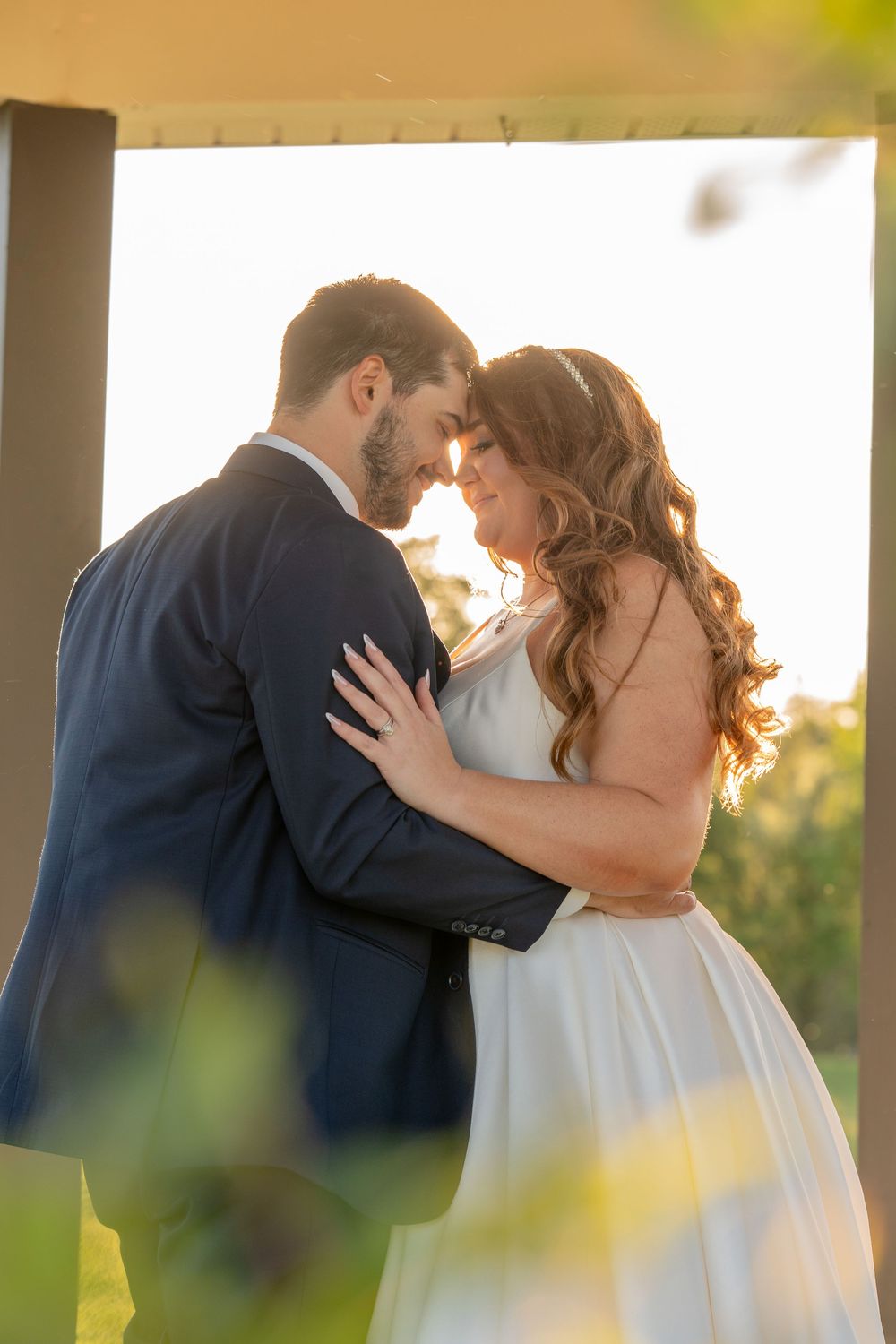A romantic moment between newlyweds sharing a kiss against a sunlit backdrop during their wedding celebration.