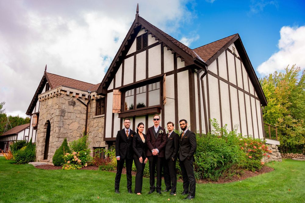 Wedding party poses outside Tudor-style venue with brown and white exterior on manicured lawn.