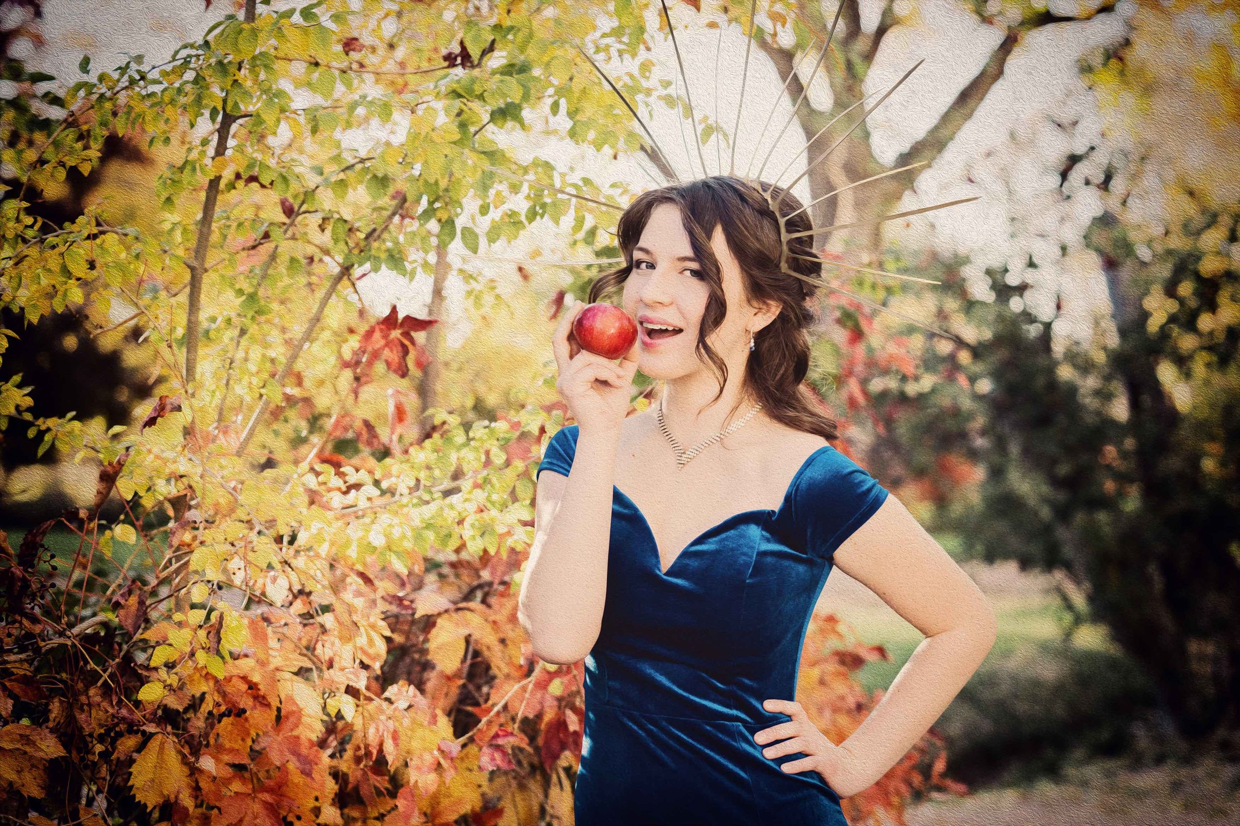 A woman in a navy blue dress poses gracefully among autumn foliage and trees.
