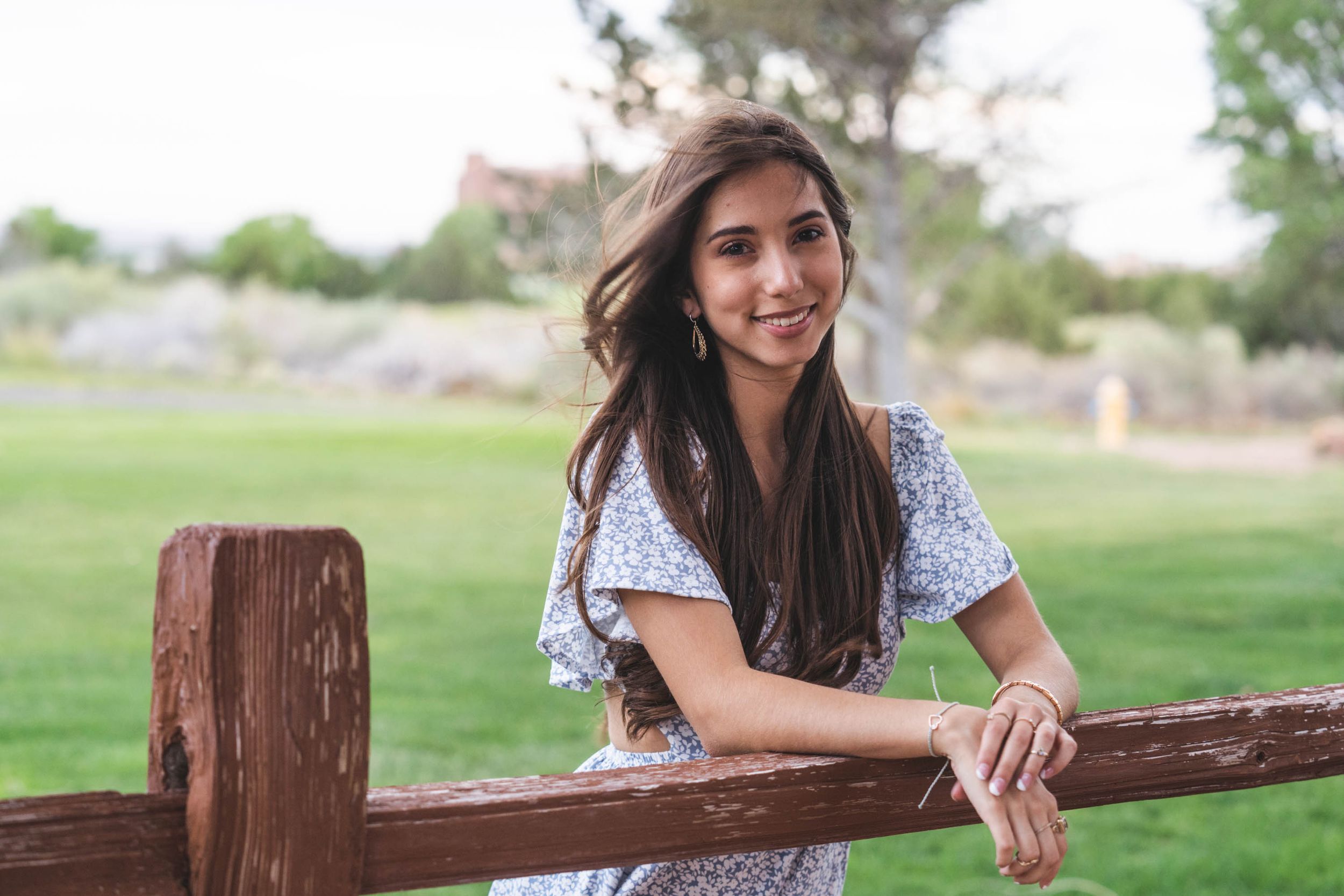 Person in blue dress leaning on wooden fence during outdoor portrait session.