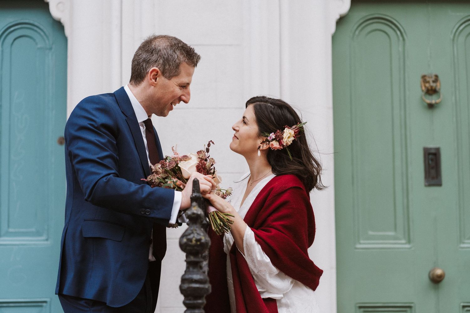 A couple in formal attire share a romantic moment in front of a teal colored door.