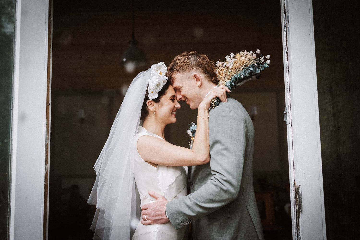 A bride and groom share an intimate moment during their wedding ceremony in a rustic indoor setting.